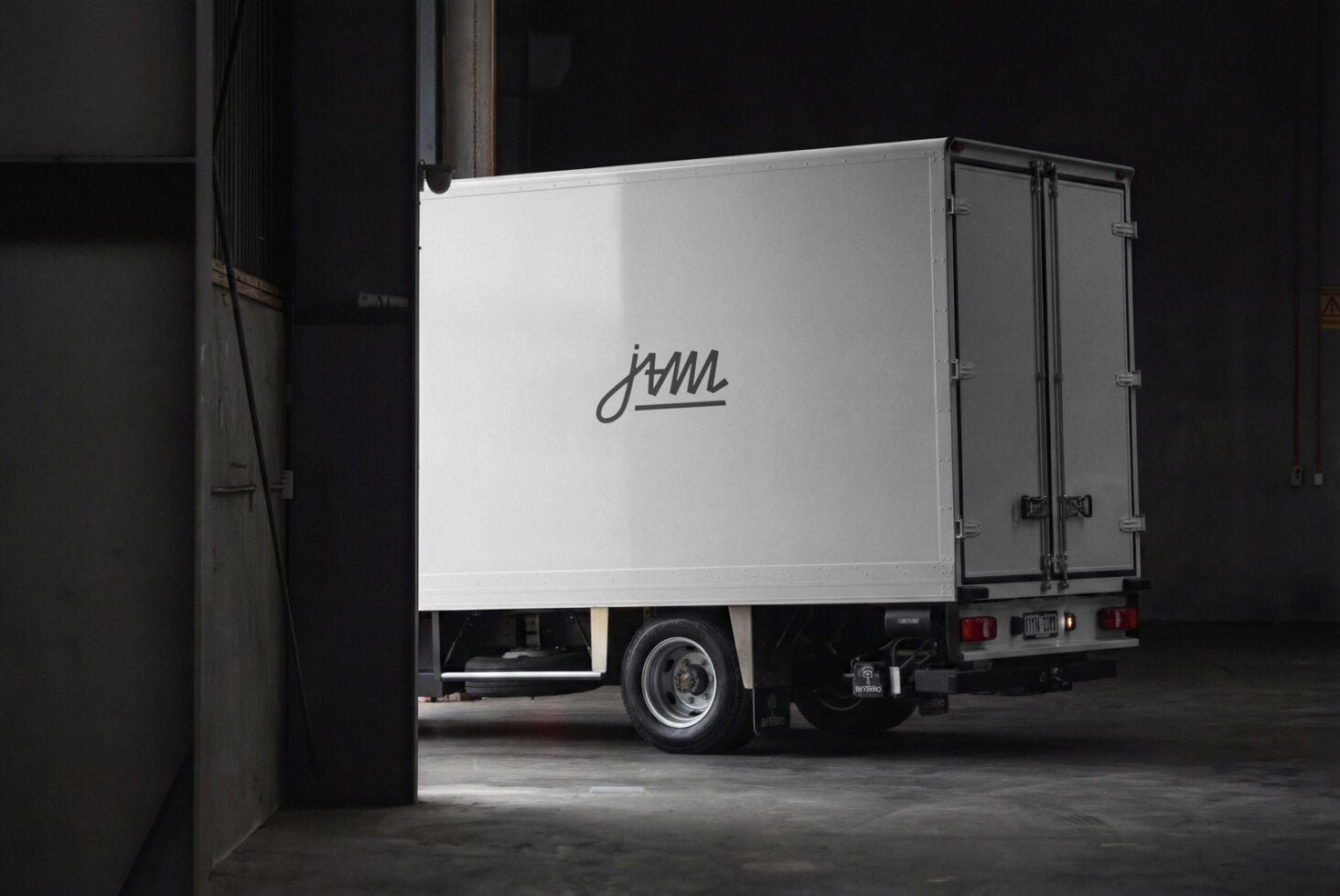 Delivery truck side view with cursive logo on white cargo box in industrial garage