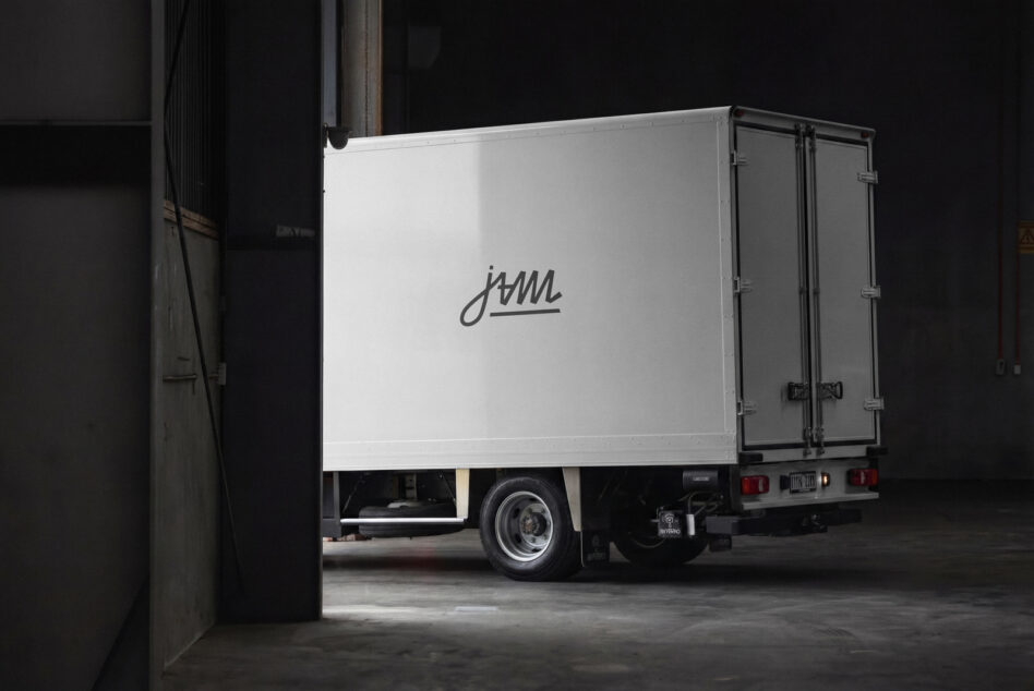 Delivery truck side view with cursive logo on white cargo box in industrial garage