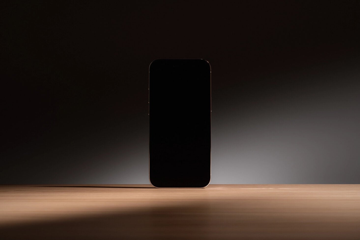 Gold-rimmed smartphone mockup standing on wooden surface with dark studio backdrop
