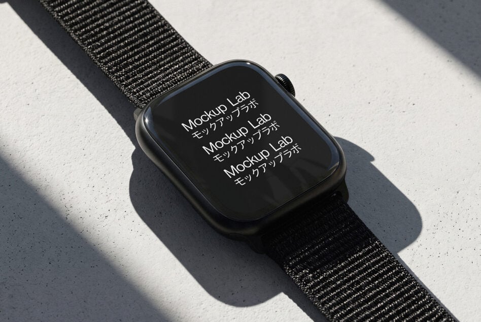 Smartwatch with dark fabric band on concrete surface, screen showing repeated text in natural daylight