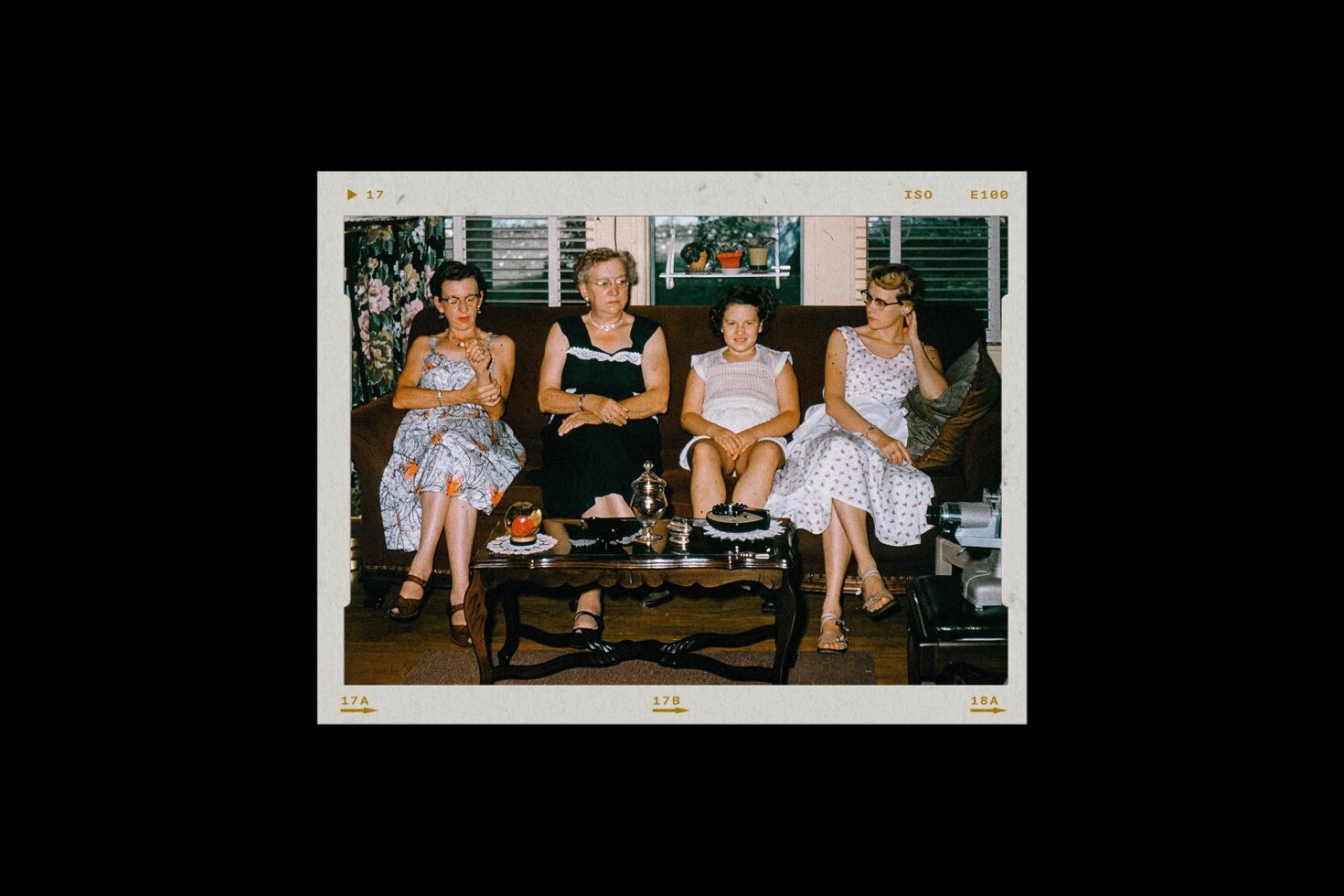 Vintage color photo of four women sitting on a dark couch in a mid-century living room with tea service