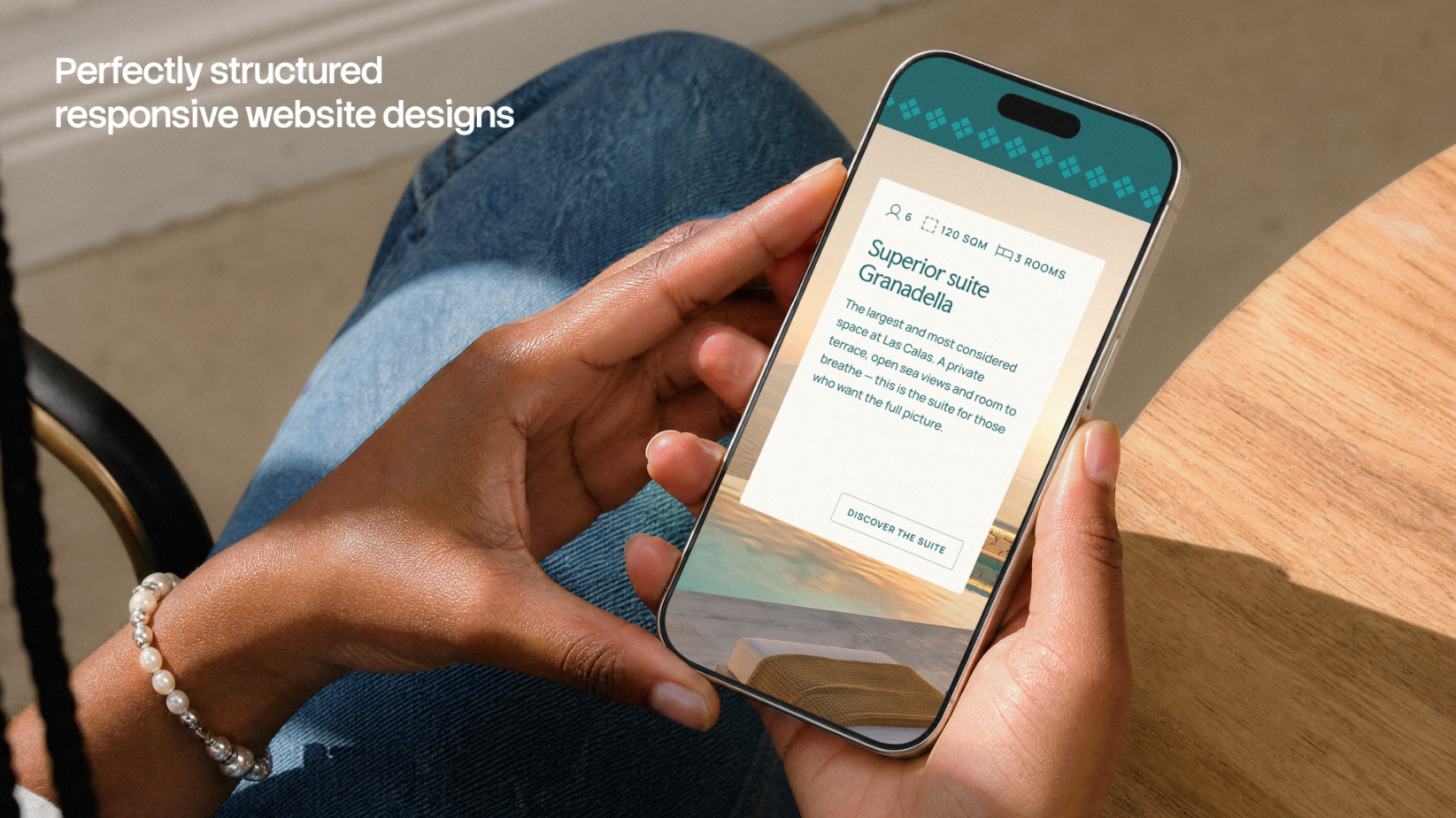Hand holding phone displaying hotel suite booking page with teal header on wooden table