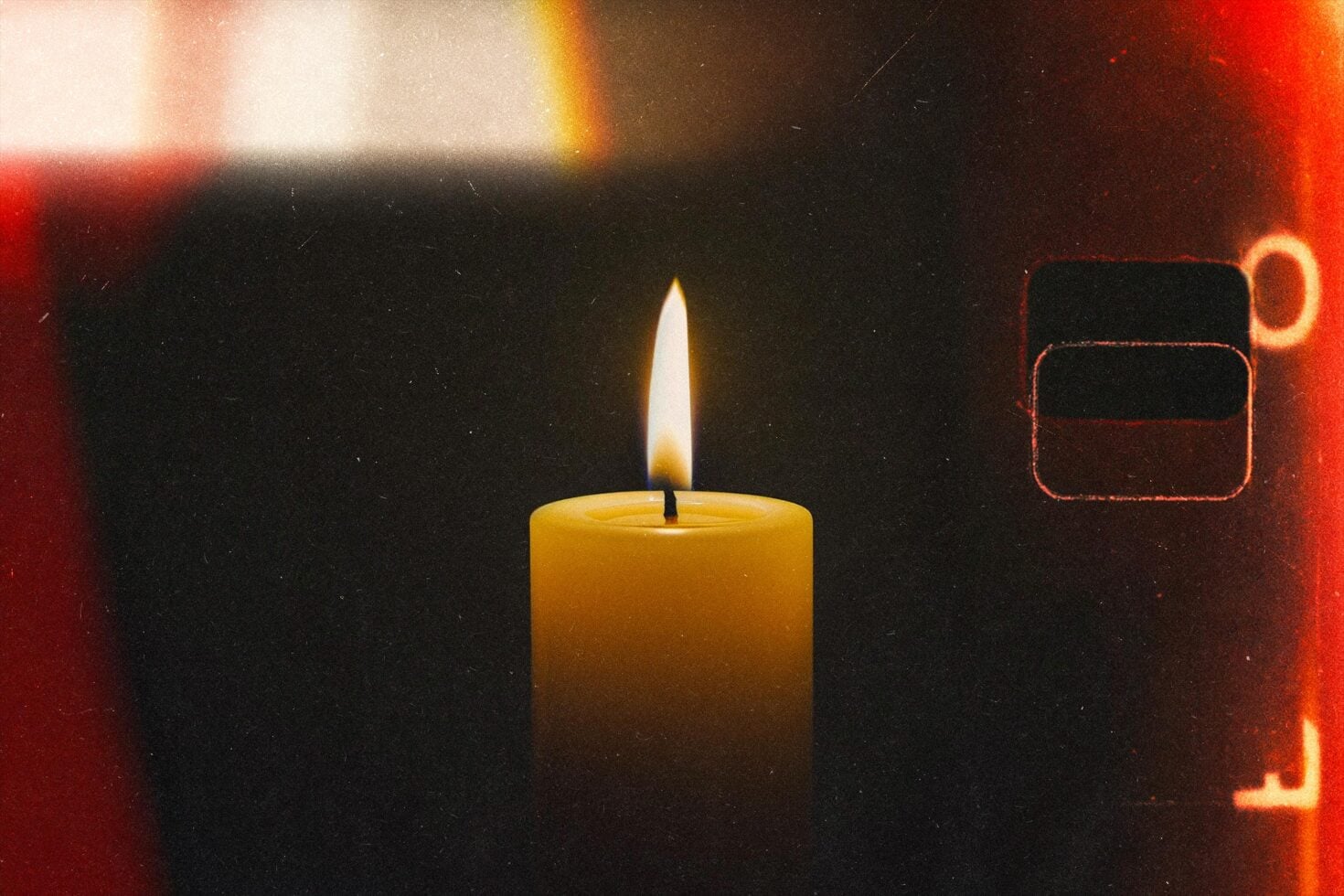 Lit candle glowing against dark background with warm red light leaks, moody film aesthetic