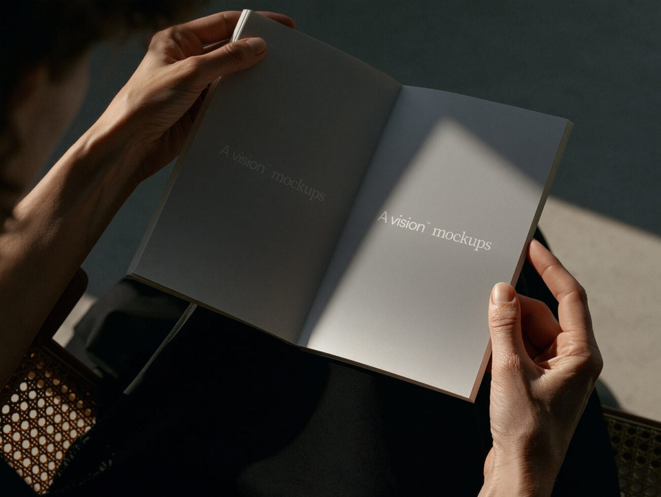 Hands holding open hardcover book with natural light casting shadows across pages