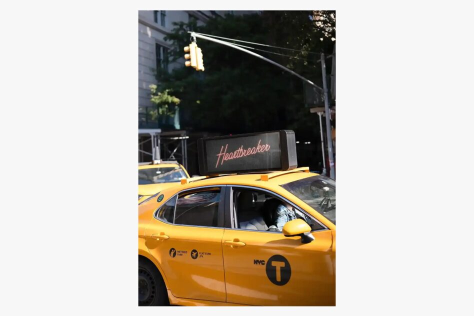 Yellow NYC taxi with Heartbreaker neon sign mounted on roof, urban street scene