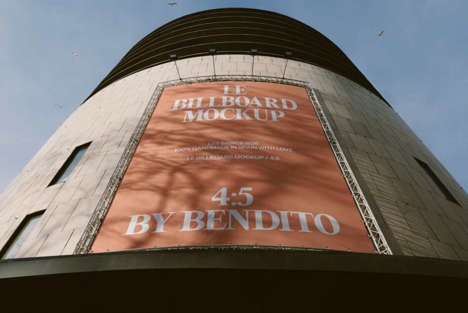 Curved billboard on cylindrical building tower with terracotta banner, metallic frame, blue sky backdrop