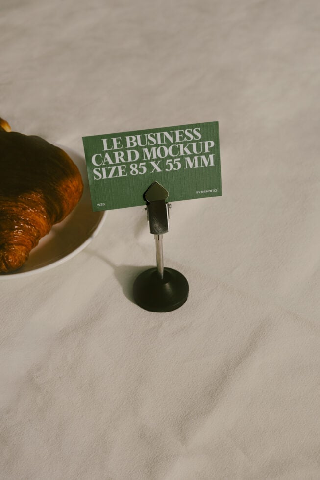 Green business card mockup on metal stand with croissant nearby, styled flat lay shot