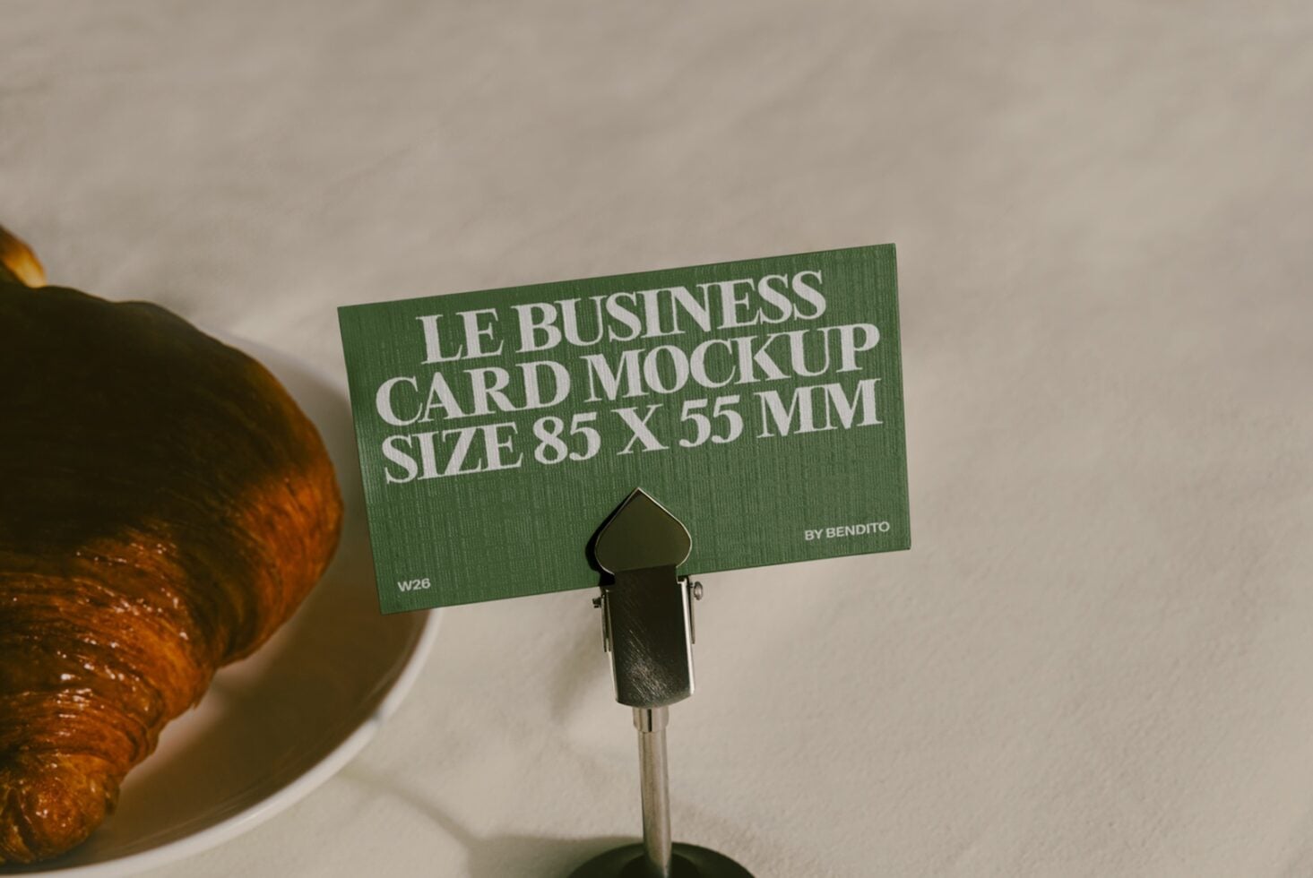 Green business card mockup 85x55mm displayed on stand next to croissant