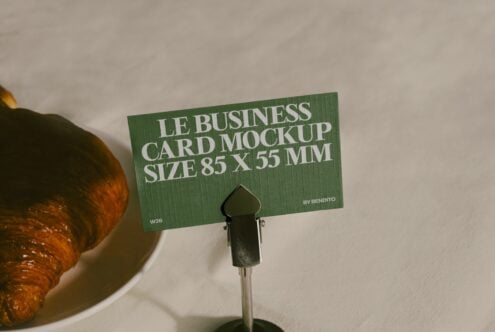 Green business card mockup 85x55mm displayed on stand next to croissant