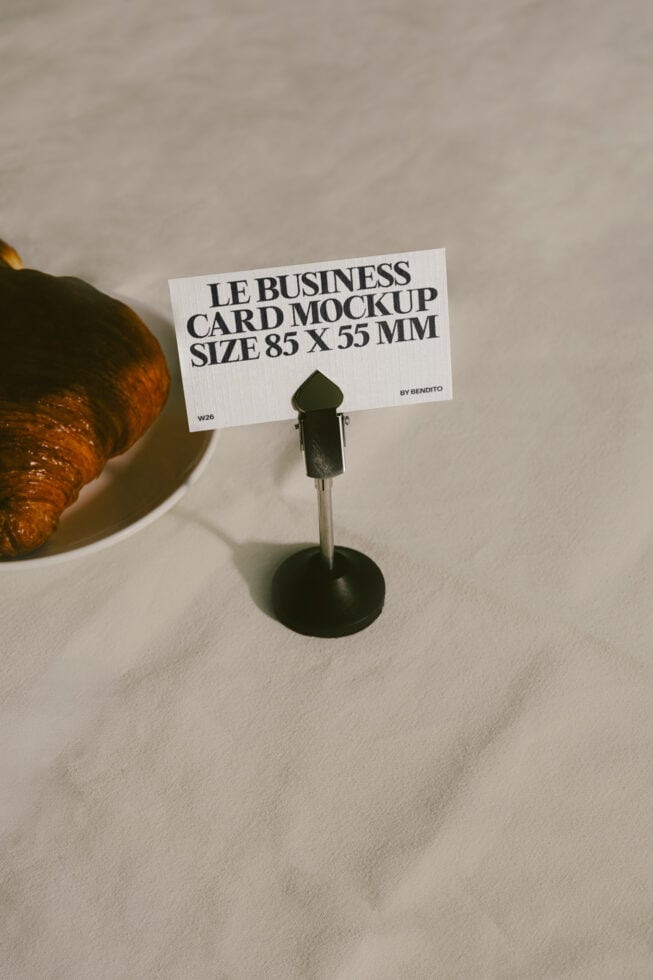 Business card mockup on metal stand with croissant, neutral backdrop, natural shadows