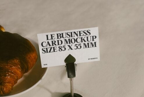 Business card mockup 85x55mm held by clip next to croissant on neutral background