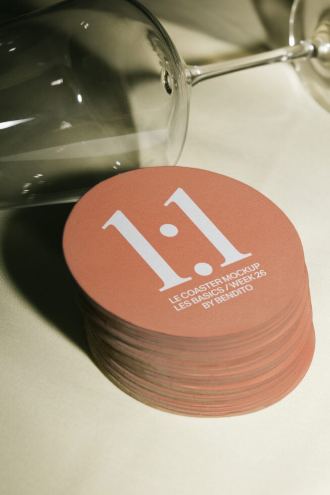 Stack of terracotta coasters with minimalist white logo design, wine glass in background