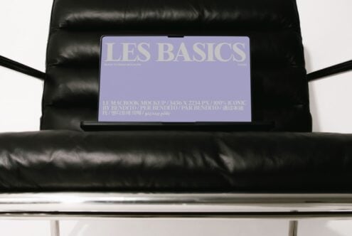 MacBook mockup on black leather couch showing Les Basics purple screen design with multilingual text