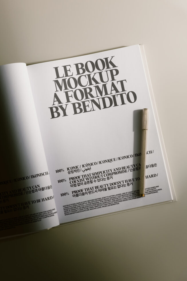 Open magazine spread showing Le Book mockup with bold typography, multilingual text, plus wooden pen on neutral background
