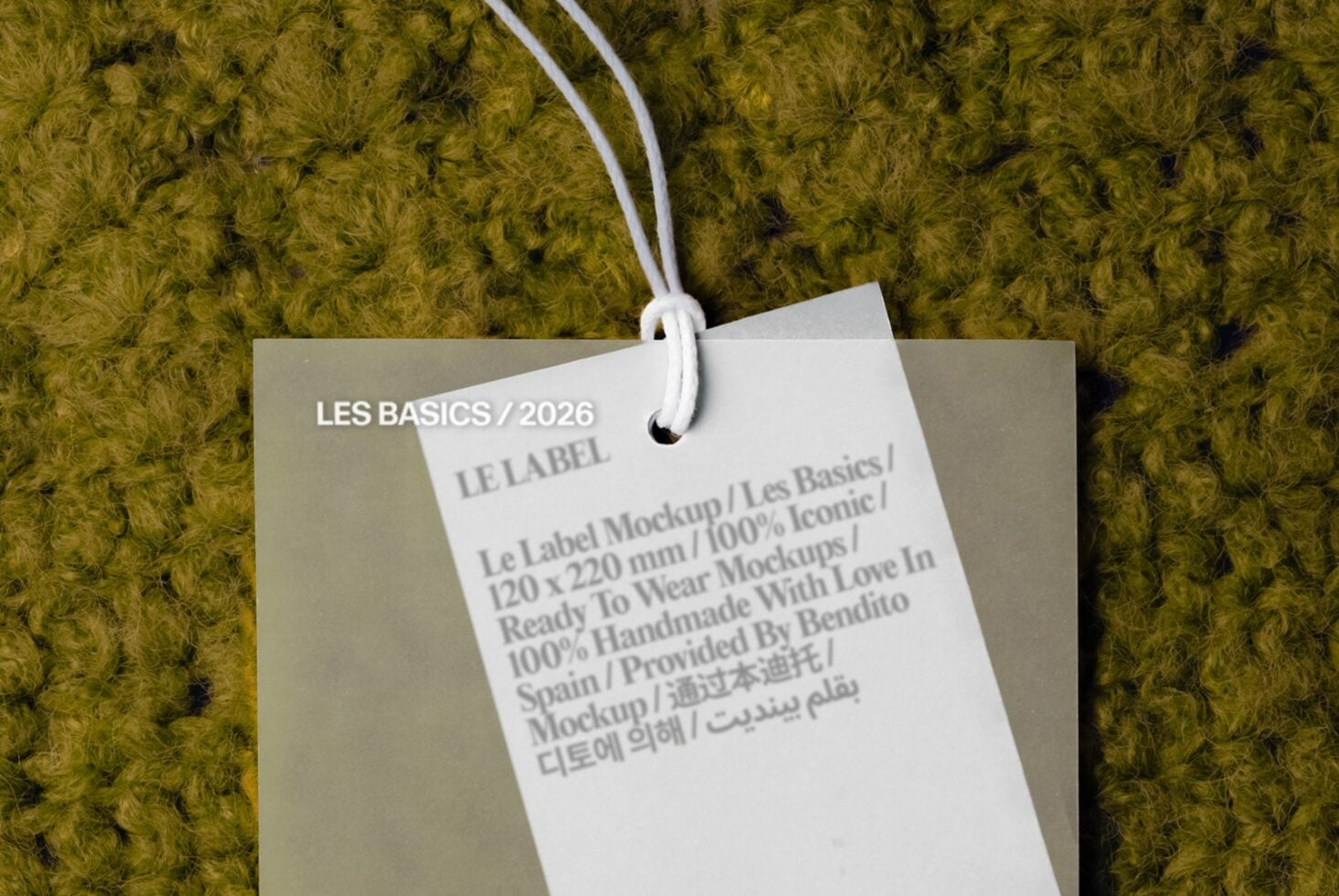 Hang tag mockup with multilingual text on cream cardstock, white cord, sitting on olive textured fabric background