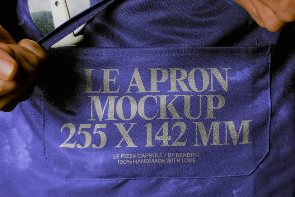 Hands opening blue apron with gold serif text showing dimensions, product details visible inside pocket