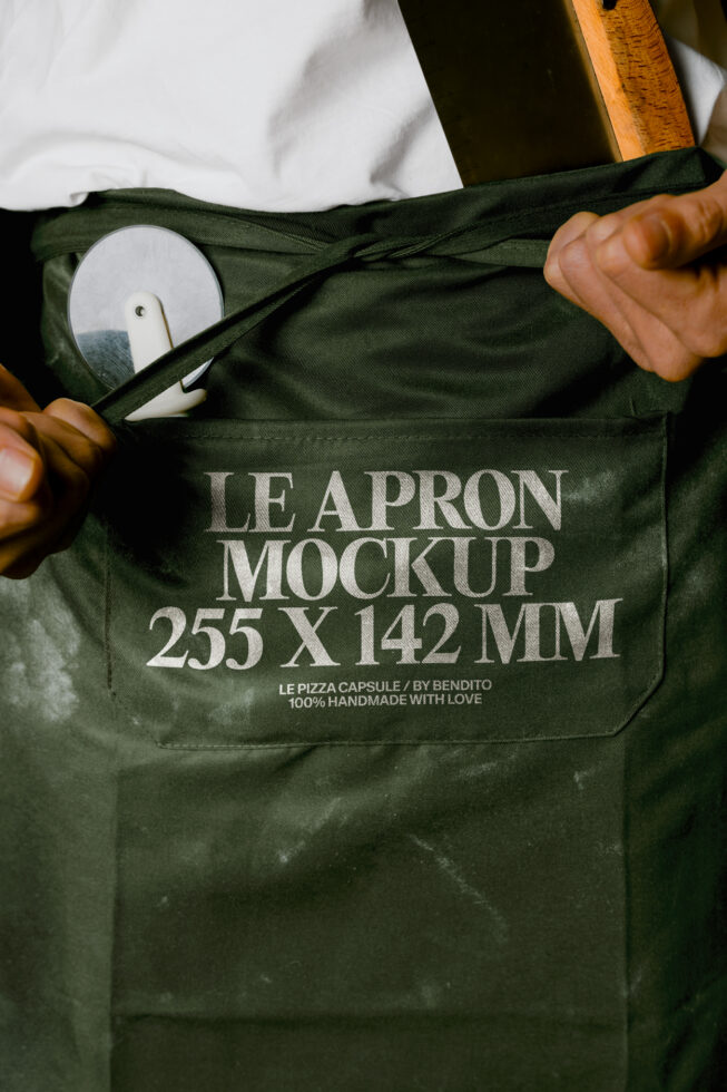 Olive apron mockup with pocket showing ceramic plate, wooden spoon propped nearby