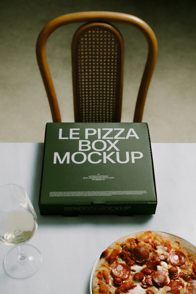 Styled pizza box mockup with green packaging on white surface, wine glass, pizza slice visible