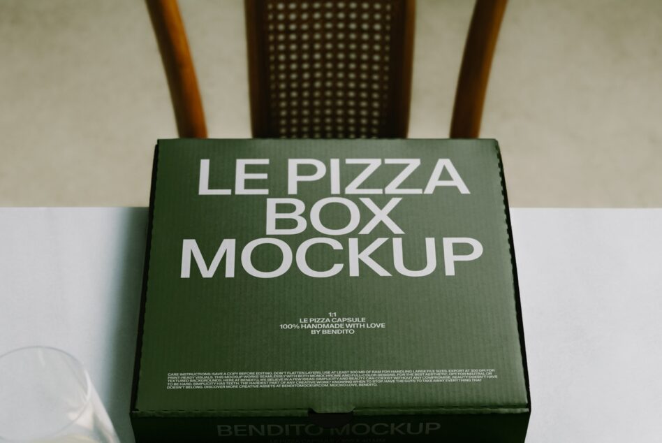 Green pizza box mockup with white text on cardboard surface, styled with wooden chairs