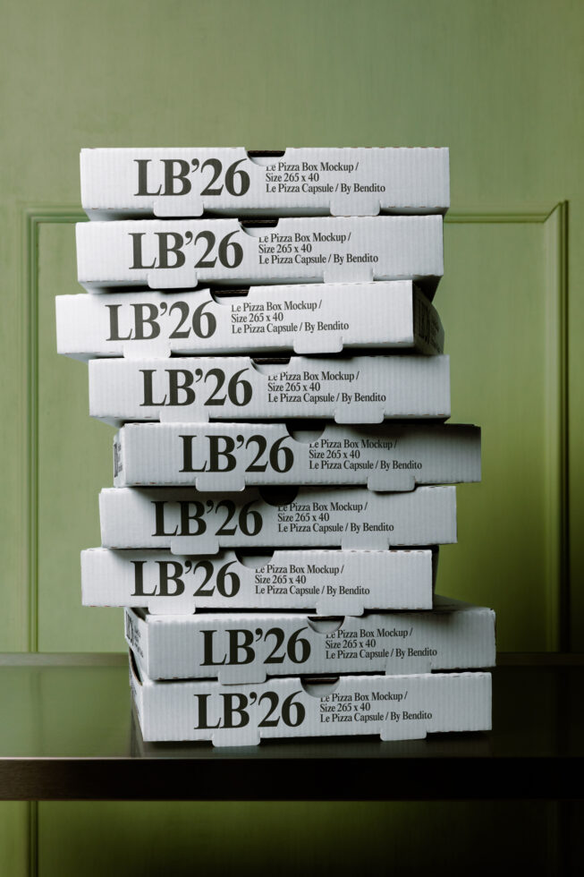 Stack of white pizza boxes labeled LB'26 against sage green paneled wall