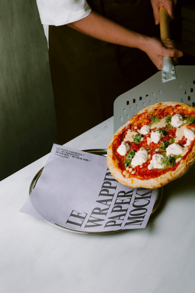 Fresh pizza on plate with open menu mockup, hands holding serving utensil
