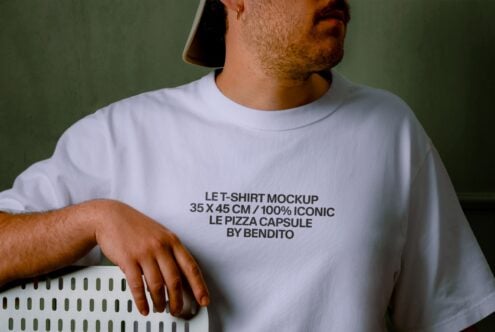 Guy wearing white tee with text design against olive green background, relaxed pose