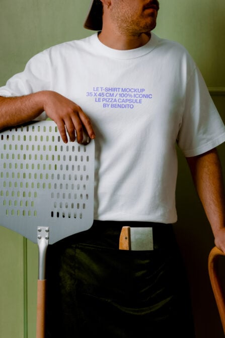 Guy in white tee holding pizza peel against sage green wall, periwinkle text mockup