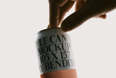 Hands holding white aluminum can mockup with black text, orange bottom band, bright studio lighting
