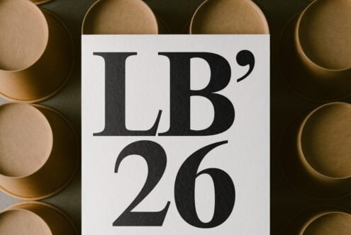 White card with bold serif typography displaying "LB'26" surrounded by stacked brass bowls on dark background