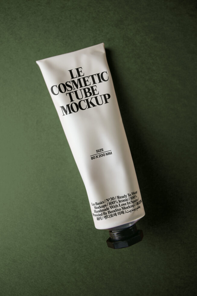 White cosmetic tube with black cap on sage green background, product text visible