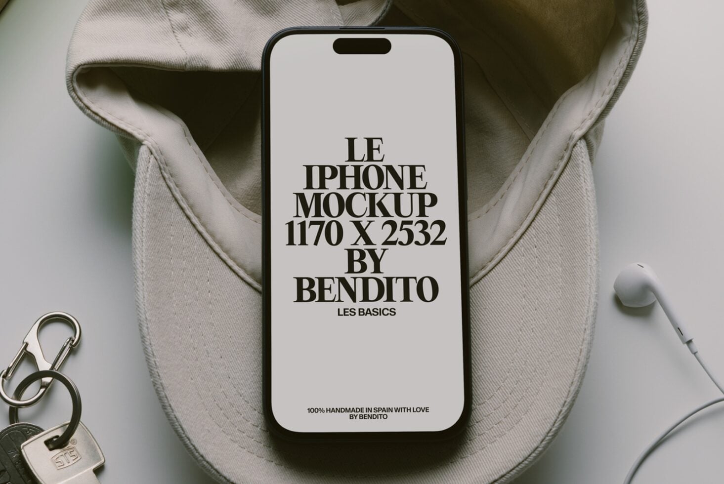 iPhone mockup on cream canvas bag with keys plus earbuds scattered around it