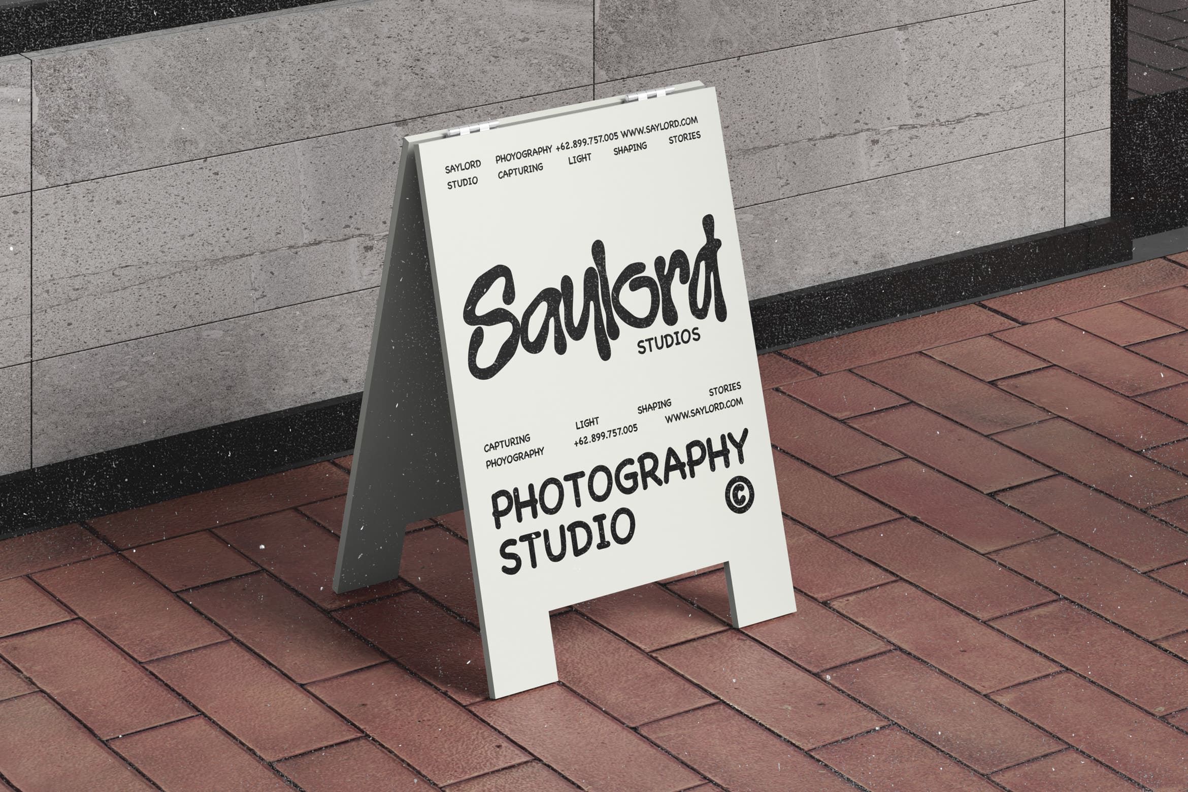 White sandwich board mockup sitting on brick pavement with Saylord Studios branding displayed