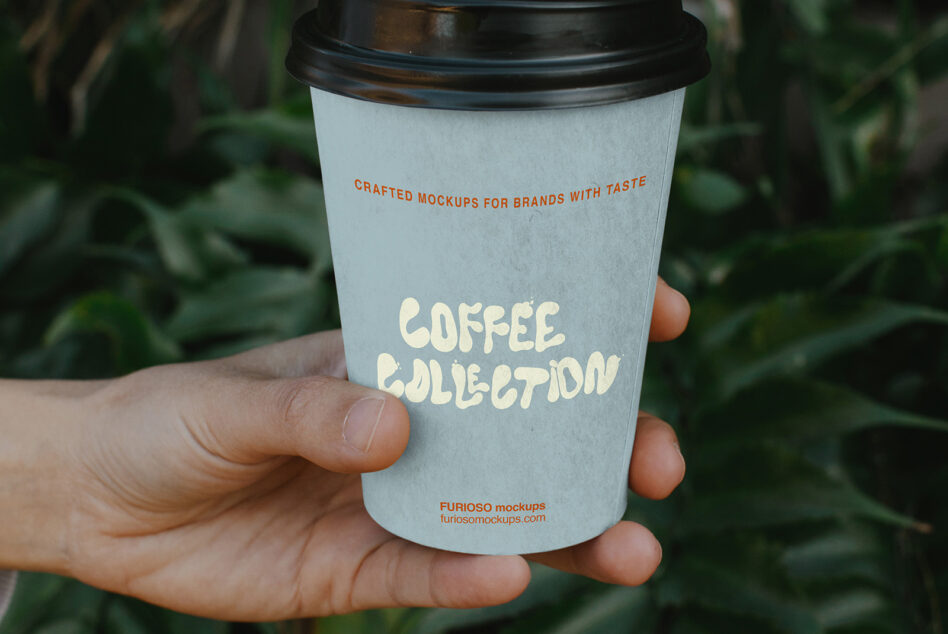 Hand holding light blue coffee cup with cream text saying "Coffee Collection" against blurred green foliage background