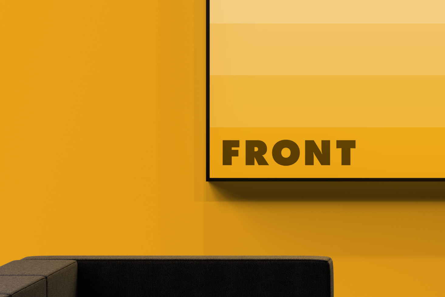 Framed poster mockup with black border on golden yellow wall with couch below