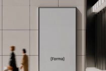Framed poster mockup on minimalist office wall with two blurred figures walking by