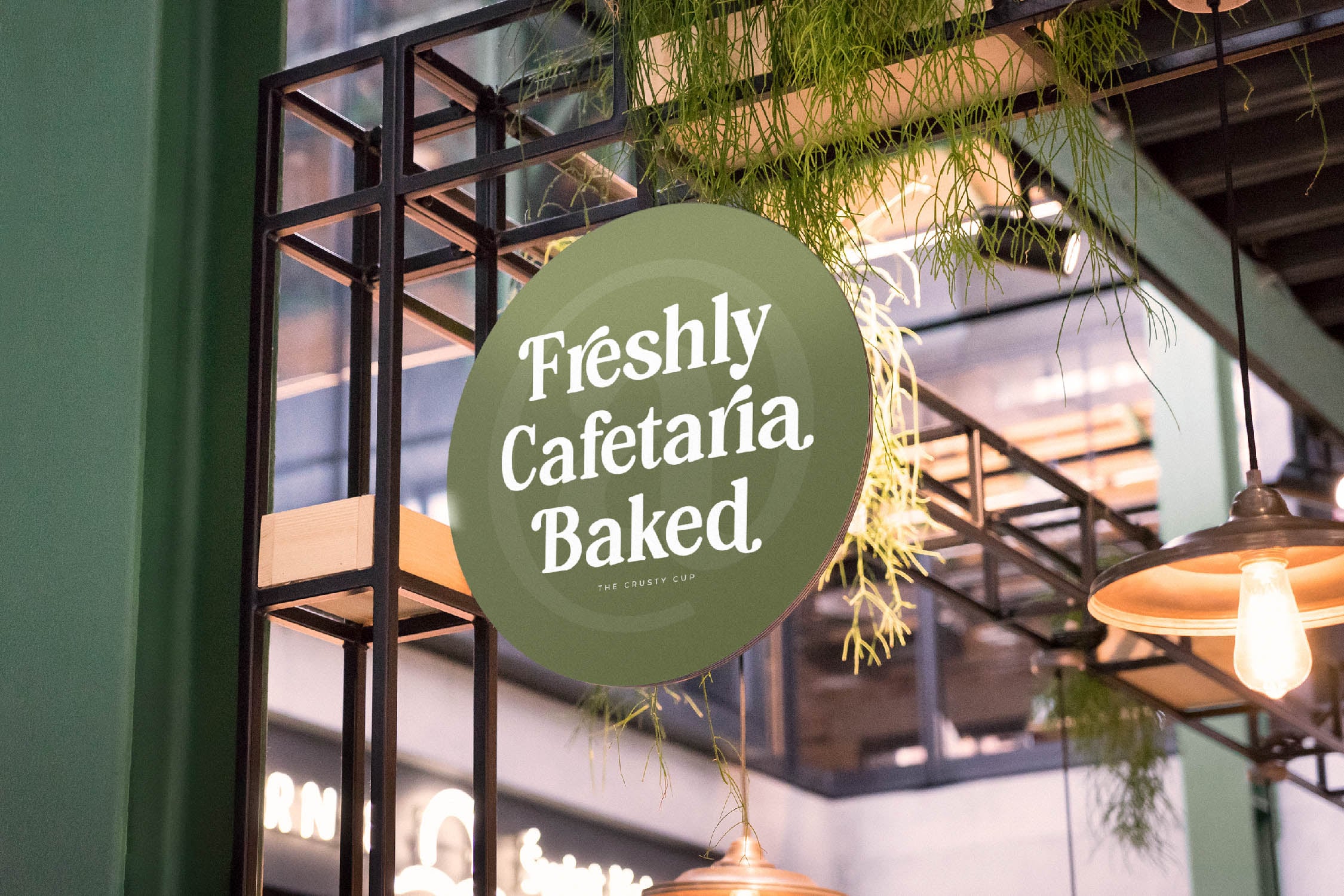 Sage green circular storefront sign for cafe with white serif typography, hanging plants, black framed window visible behind