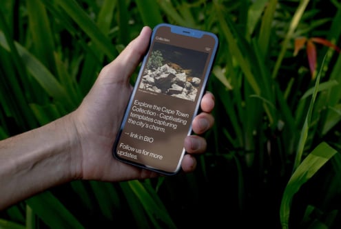 Hand holding blue phone displaying Cape Town Collection travel app mockup with nature background