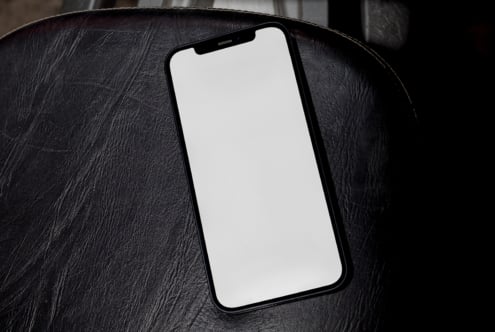 Black iPhone on dark leather surface with blank screen ready for your design