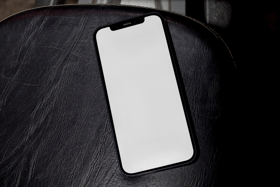 Black iPhone on dark leather surface with blank screen ready for your design