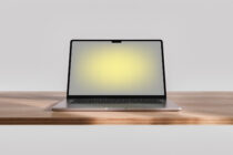 Silver laptop on wooden desk with soft yellow screen glow against gray background