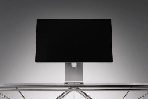 Sleek desktop monitor mockup with black screen on metallic stand, minimal studio setup