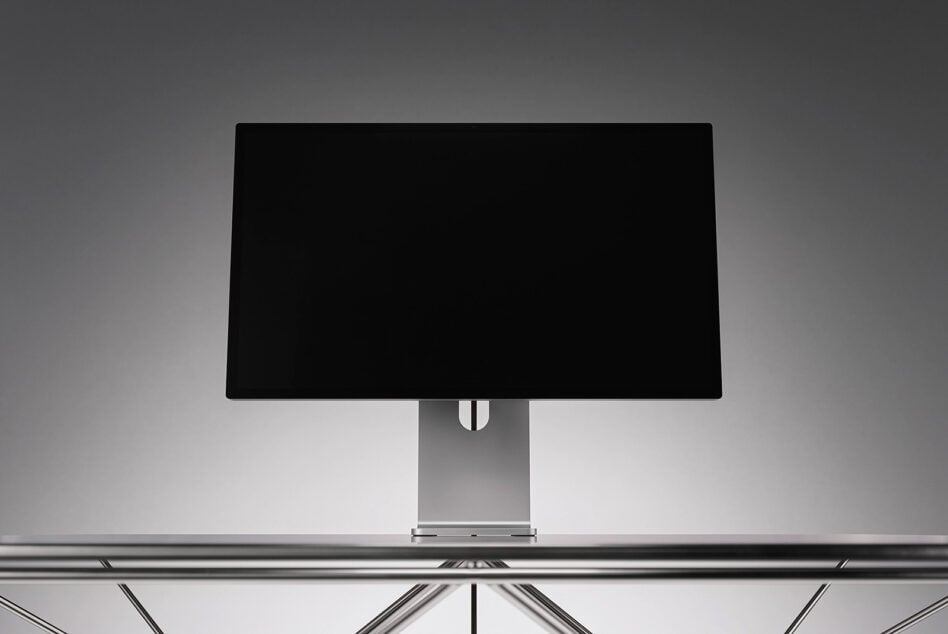 Sleek desktop monitor mockup with black screen on metallic stand, minimal studio setup