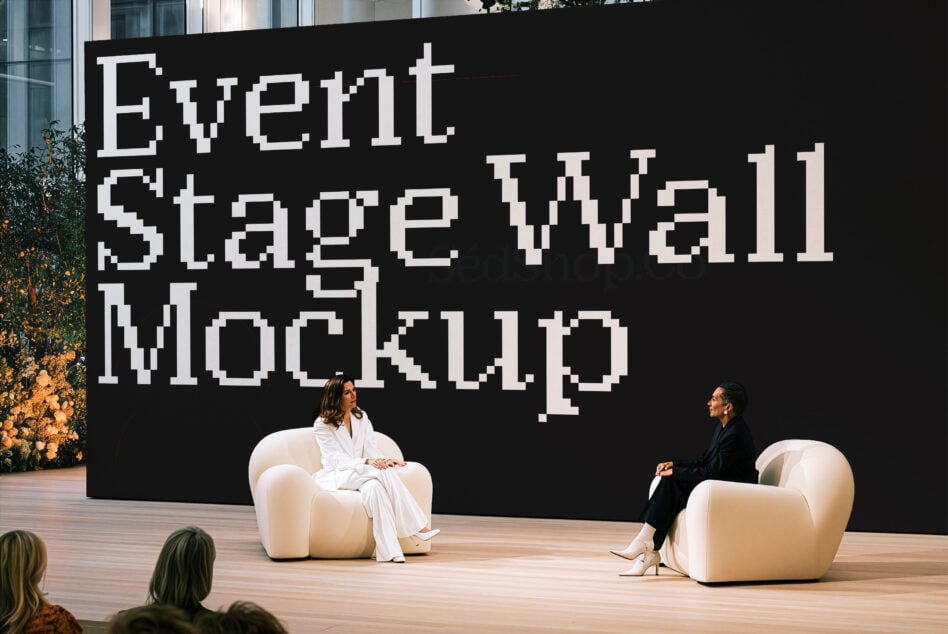 Large event stage setup with two people seated on cream curved chairs talking in front of pixelated white text on black backdrop
