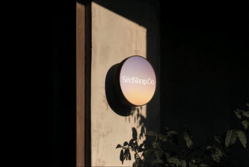 Circular storefront sign with gradient display mounted on textured cream wall, dramatic shadow overlay