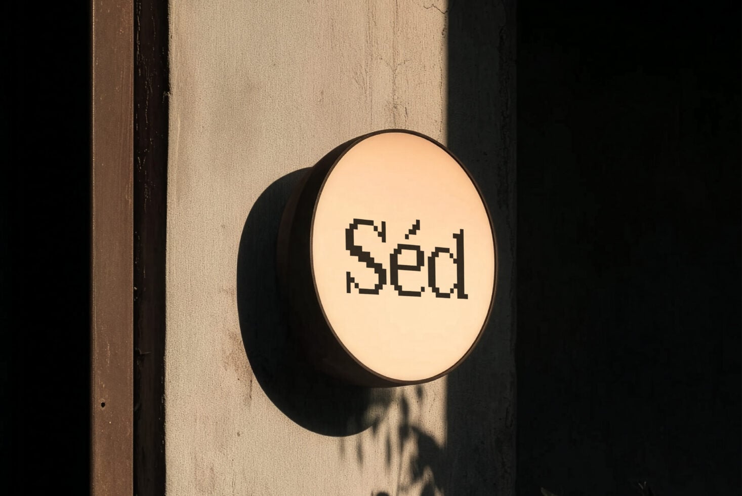 Circular storefront sign with pixel font text mounted on weathered beige wall between dark trim