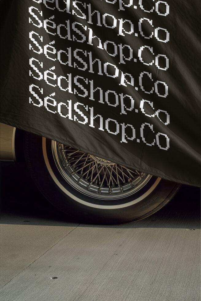 Luxury car wheel with repeated monospace text on black fabric above it, cinematic lighting