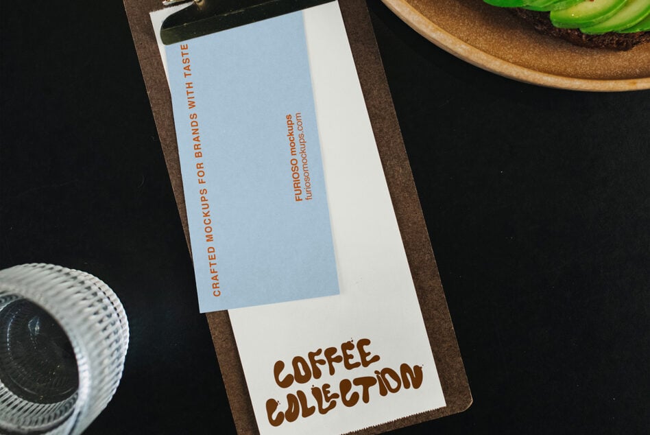 Flat lay of branded coffee sleeve mockup with light blue panel, cream background, orange text on dark wood surface next to avocado toast bowl