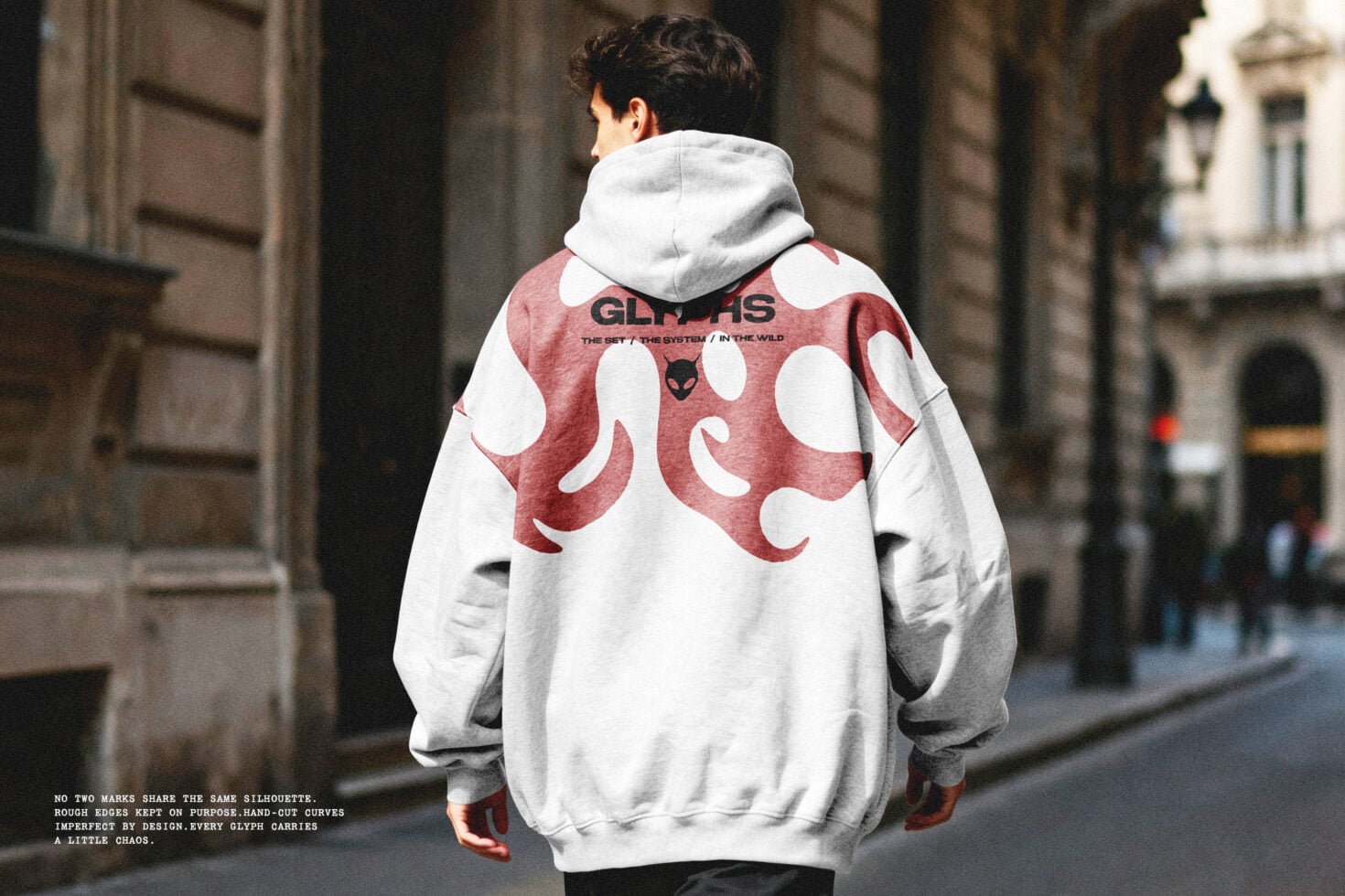 Guy walking away in white hoodie with red back print, urban street setting