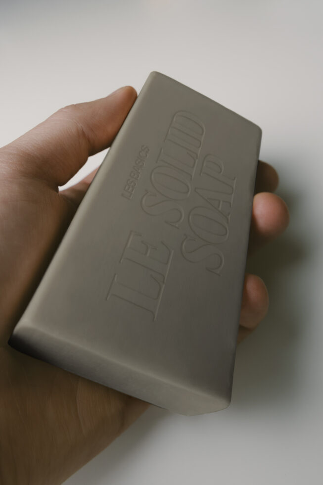 Hand holding sage green soap bar with embossed text on neutral background