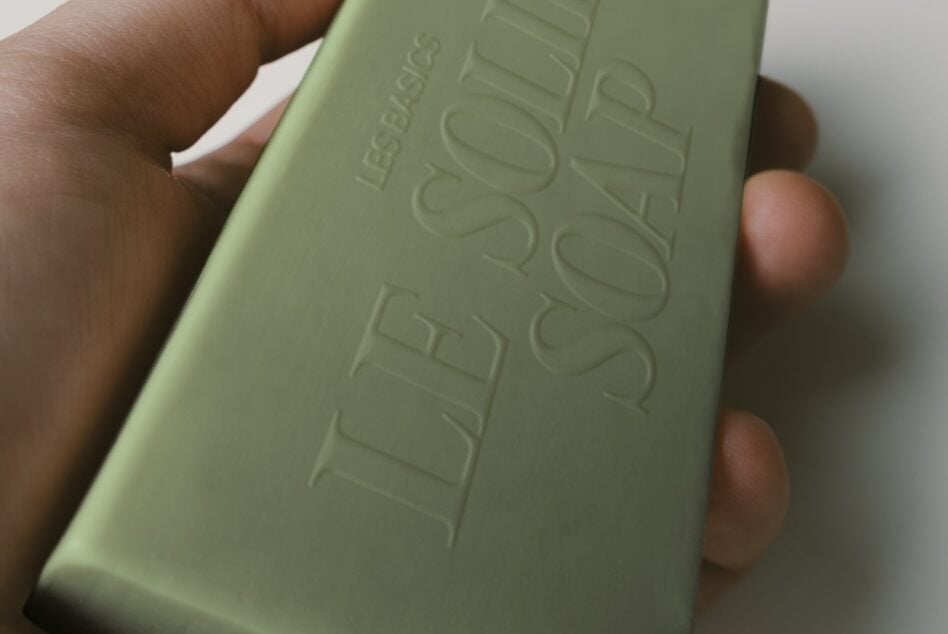 Sage green soap bar with debossed branding held in someone's hand, close up shot showing texture